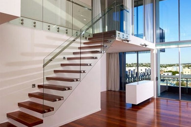Diseño de escalera recta actual grande sin contrahuella con escalones de madera y barandilla de vidrio