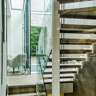 Diseño de escalera en U, actual, pequeña, con escalones de madera, contrahuellas de metal y barandilla de vidrio