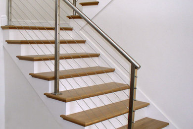 Imagen de escalera en U actual de tamaño medio con escalones de madera, contrahuellas de madera pintada y barandilla de cable