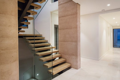 На фото: лестница на больцах в современном стиле с деревянными ступенями и стеклянными перилами без подступенок с