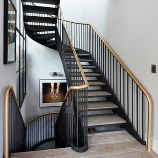 Large traditional wood curved metal railing staircase in London with open risers.