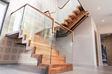 Ejemplo de escalera suspendida actual grande con escalones de madera, contrahuellas de madera y barandilla de vidrio