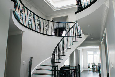 Example of a large transitional wooden curved staircase design in Toronto with painted risers