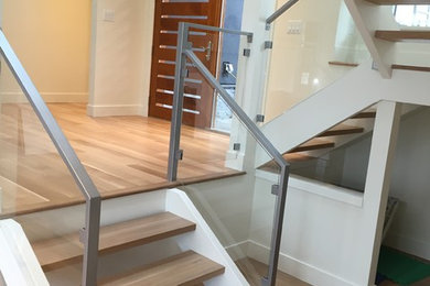 Ejemplo de escalera en U actual grande sin contrahuella con escalones de madera y barandilla de vidrio