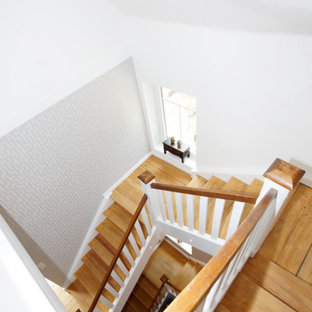 Immagine di una grande scala minimal con pedata in legno, alzata in legno, parapetto in legno e carta da parati