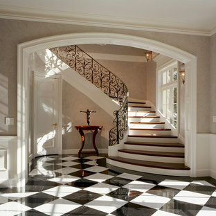 Imagen de escalera curva, clásica, grande, con escalones de madera, contrahuellas de madera pintada y barandilla de metal