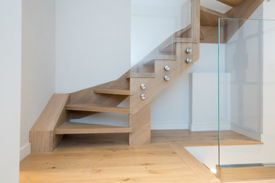 Modern inredning av en mellanstor flytande trappa i trä, med öppna sättsteg och räcke i glas
