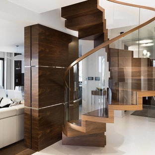 Trendy wooden spiral glass railing staircase photo in New York with wooden risers