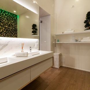 Immagine di una stanza da bagno contemporanea con ante lisce, ante bianche, piastrelle bianche, pareti bianche, pavimento in legno massello medio, lavabo integrato, pavimento marrone e top bianco