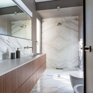 Immagine di una stanza da bagno con doccia design con ante in legno bruno, doccia a filo pavimento, piastrelle di marmo, top bianco, ante lisce, bidè, pareti grigie, lavabo integrato, pavimento grigio e porta doccia a battente