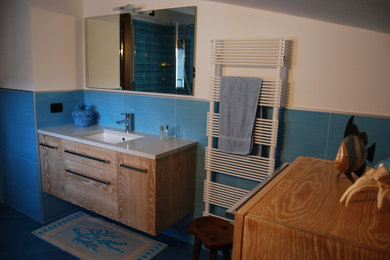 他の地域にあるお手頃価格のコンテンポラリースタイルのおしゃれなバスルーム (浴槽なし) (フラットパネル扉のキャビネット、淡色木目調キャビネット、青いタイル、セラミックタイル、白い壁、セラミックタイルの床、オーバーカウンターシンク、珪岩の洗面台、青い床、白い洗面カウンター、洗面台1つ、フローティング洗面台、折り上げ天井) の写真