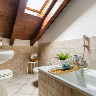 Immagine di una stanza da bagno mediterranea di medie dimensioni con vasca da incasso, bidè, piastrelle beige, pareti bianche, lavabo a colonna e pavimento beige