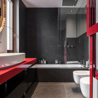 Esempio di una stanza da bagno padronale minimal con pavimento con piastrelle in ceramica, lavabo a bacinella, top in vetro, ante lisce, ante nere, vasca sottopiano, vasca/doccia, bidè, piastrelle nere, pavimento grigio, porta doccia scorrevole e top rosso