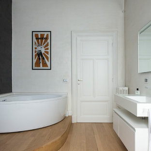 Esempio di una stanza da bagno minimal con ante lisce, ante bianche, vasca ad angolo, pareti bianche, parquet chiaro, lavabo sospeso, pavimento marrone e top bianco