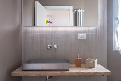 バーリにあるコンテンポラリースタイルのおしゃれな浴室 (壁掛け式トイレ、グレーのタイル、グレーの壁、ベッセル式洗面器、木製洗面台、グレーの床、ベージュのカウンター) の写真