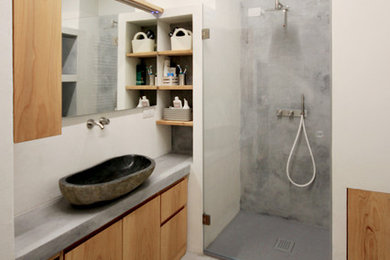 Kleines Modernes Duschbad mit Kassettenfronten, hellen Holzschränken, bodengleicher Dusche, Wandtoilette mit Spülkasten, beigen Fliesen, beiger Wandfarbe, Aufsatzwaschbecken, grauem Boden, Falttür-Duschabtrennung und grauer Waschtischplatte in Sonstige