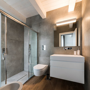 Immagine di una stanza da bagno padronale minimal di medie dimensioni con ante lisce, ante bianche, doccia alcova, bidè, pareti grigie, pavimento in legno massello medio, lavabo sospeso, pavimento marrone, porta doccia scorrevole e piastrelle grigie