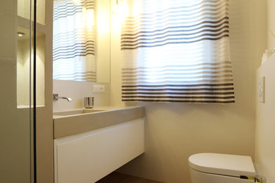 На фото: ванная комната в стиле модернизм с плоскими фасадами, белыми фасадами, раздельным унитазом, бежевой плиткой, керамогранитной плиткой, бежевыми стенами, паркетным полом среднего тона, душевой кабиной, накладной раковиной, столешницей из бетона и бежевым полом с