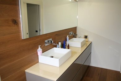 Imagen de cuarto de baño contemporáneo de tamaño medio con armarios con paneles lisos, puertas de armario marrones, paredes blancas, suelo de madera pintada, aseo y ducha y encimera de vidrio