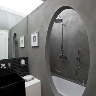 Idee per una stanza da bagno padronale design con ante lisce, ante bianche, vasca sottopiano, vasca/doccia, piastrelle grigie, pareti grigie, pavimento nero e top bianco