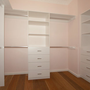 Modelo de armario vestidor de mujer, minimalista, de tamaño medio, con armarios con paneles lisos, puertas de armario blancas y suelo de madera en tonos medios