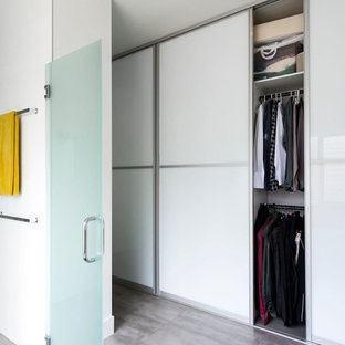 Immagine di una cabina armadio unisex design di medie dimensioni con ante di vetro, ante bianche e pavimento in cemento