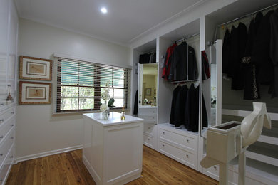 Imagen de armario vestidor unisex clásico de tamaño medio con armarios estilo shaker, puertas de armario blancas y suelo de madera clara