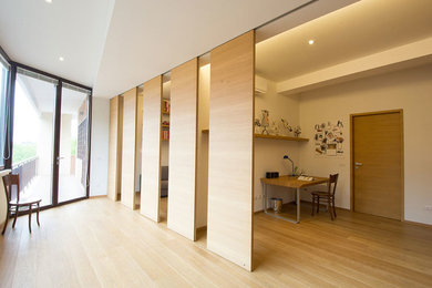 Foto på ett stort funkis hemmastudio, med vita väggar, ljust trägolv och ett fristående skrivbord
