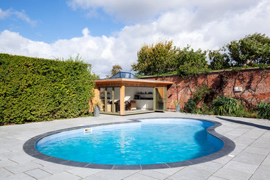 На фото: наземный бассейн среднего размера, в форме фасоли на заднем дворе в современном стиле с домиком у бассейна и покрытием из каменной брусчатки