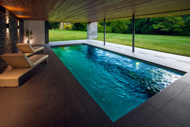 This is an example of a medium sized modern back rectangular infinity swimming pool in Kent with a pool house and tiled flooring.