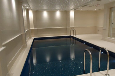 This is an example of a large contemporary indoor rectangular swimming pool in London with a pool house and natural stone paving.