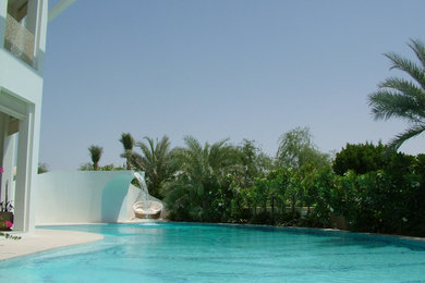 This is an example of a large modern back custom shaped infinity swimming pool in Other with a water feature and concrete slabs.