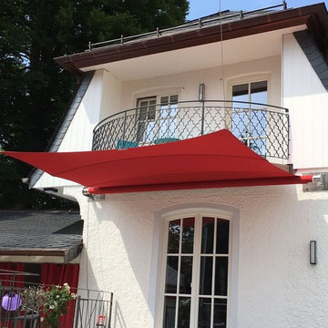 Ein rotes Sonnensegel für eine weiße Landhaus-Villa am Chiemsee