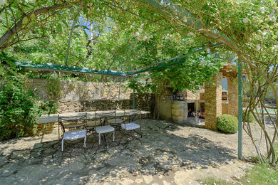 Exemple d'une grande terrasse arrière méditerranéenne avec une cuisine d'été, des pavés en pierre naturelle et une pergola.