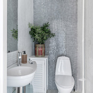 Foto på ett litet skandinaviskt toalett, med en toalettstol med hel cisternkåpa, grå kakel, mosaik, grå väggar, ett väggmonterat handfat och flerfärgat golv