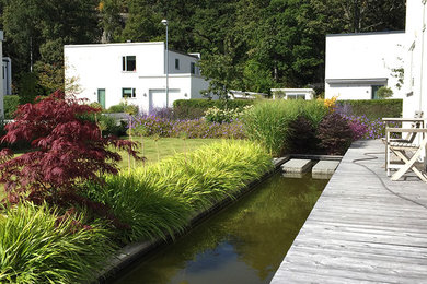Réalisation d'un grand jardin à la française avant minimaliste l'été avec un point d'eau, une exposition ensoleillée et une terrasse en bois.