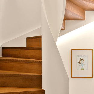 Imagen de escalera curva, actual, pequeña, con escalones de madera, contrahuellas de madera y barandilla de madera