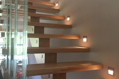 Ejemplo de escalera en L actual grande con escalones de madera y barandilla de vidrio