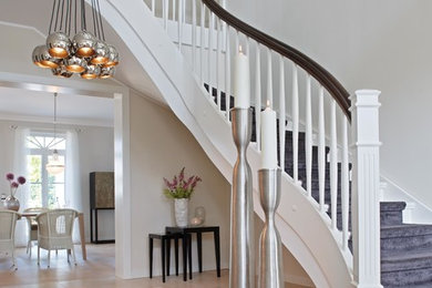 Пример оригинального дизайна: большая изогнутая лестница в стиле неоклассика (современная классика) с крашенными деревянными ступенями и крашенными деревянными подступенками