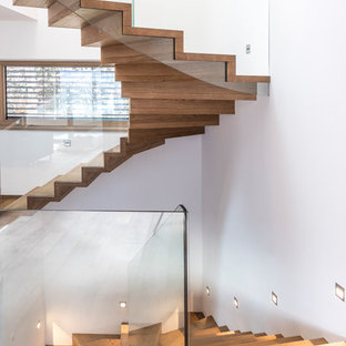 Ispirazione per una scala curva design con pedata in legno, alzata in legno e parapetto in vetro
