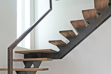 Kleine Industrial Treppe in U-Form mit gebeizten Holz-Treppenstufen, offenen Setzstufen und Stahlgeländer in Sonstige