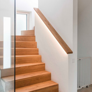 Cette photo montre un escalier courbe tendance de taille moyenne avec des marches en bois, des contremarches en bois, un garde-corps en verre et un mur en parement de brique.