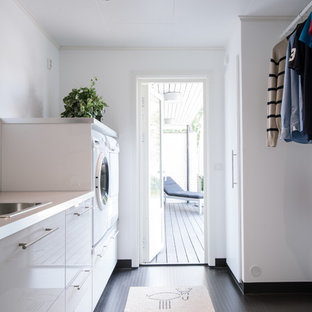 Idéer för funkis parallella vitt tvättstugor, med en nedsänkt diskho, släta luckor, vita skåp, vita väggar, en tvättmaskin och torktumlare bredvid varandra och svart golv