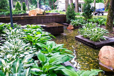 Aménagement d'un grand jardin contemporain l'été avec un bassin, une exposition partiellement ombragée, une pente, une colline ou un talus et des pavés en pierre naturelle.