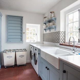 Immagine di una piccola sala lavanderia country con lavello stile country, ante blu, top in granito, pareti bianche, pavimento in terracotta, lavatrice e asciugatrice affiancate, ante in stile shaker, pavimento rosso e top bianco