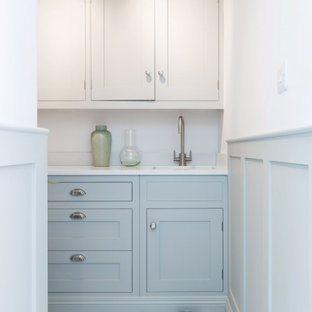 Esempio di una piccola lavanderia multiuso country con lavello integrato, ante lisce, ante blu, top in quarzite, pareti bianche, pavimento con piastrelle in ceramica, lavatrice e asciugatrice a colonna, pavimento bianco e top bianco