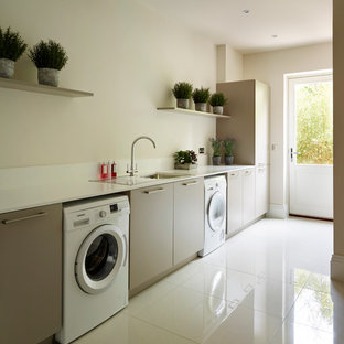 Immagine di una lavanderia minimal con ante lisce, lavatrice e asciugatrice affiancate, pareti beige, pavimento bianco, ante grigie e lavello da incasso