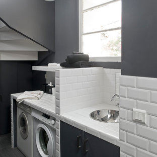 Exemple d'une buanderie linéaire tendance dédiée et de taille moyenne avec un mur gris, des machines côte à côte, un plan de travail en carrelage, un évier encastré et un sol en bois peint.