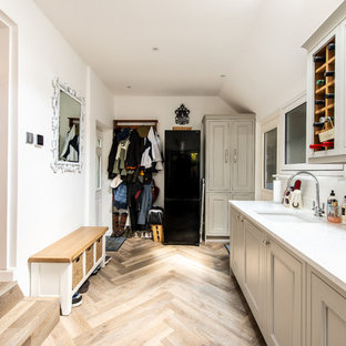 This is an example of a medium sized classic single-wall utility room in Kent with a submerged sink, recessed-panel cabinets, grey cabinets, white walls, light hardwood flooring and white worktops.