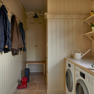 Foto på ett mellanstort lantligt beige parallellt grovkök, med en rustik diskho, luckor med infälld panel, beige skåp, bänkskiva i kvarts, beige stänkskydd, beige väggar, kalkstensgolv, en tvättmaskin och torktumlare bredvid varandra och beiget golv